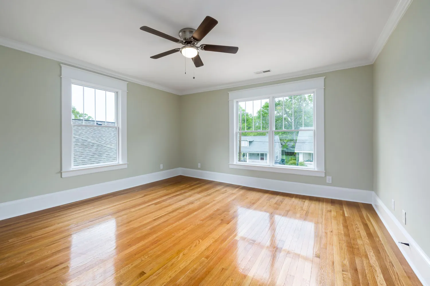An empty, clean room with wood floors and bright windows